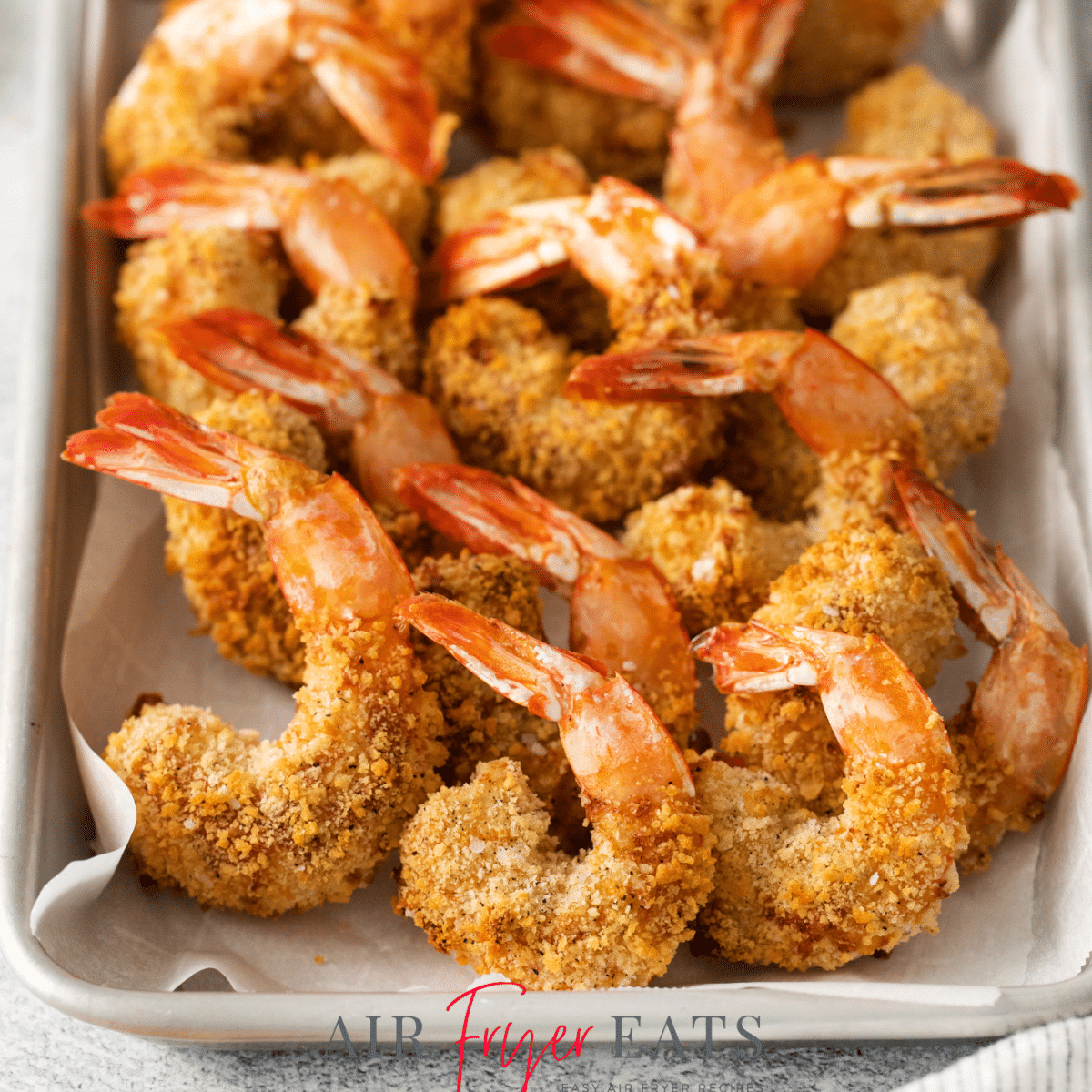 air fried crunchy breaded shrimp with tails, on a platter lined with parchment paper