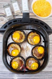 Vertical photo with air fryer breakfast bites in an air fryer basket with sausage patties and eggs added to each cup