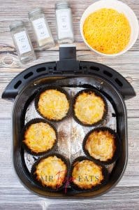 vertical image of jumbo muffin liners in an air fryer basket with hash brown potatoes lining them, cooked