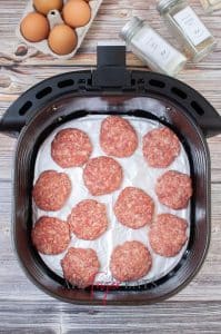 vertical photo of sausage meat patties in an air fryer basket for air fryer breaksfast bites