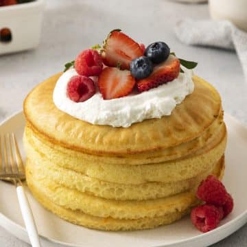 closeup of round formed pancakes that were cooked in an air fryer, topped with cream and berries.