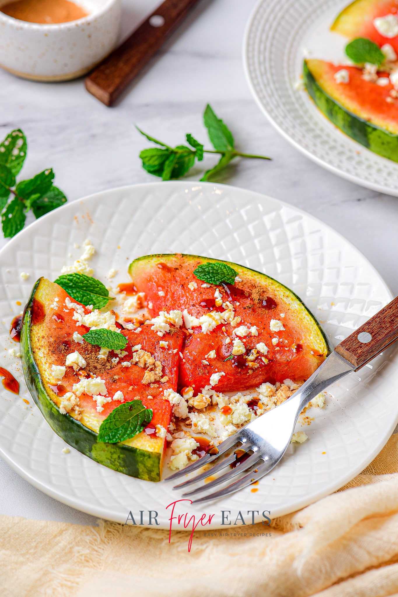 two pieces of air fried watermelon topped with fresh mint, dressing, and feta cheese, on a plate. 