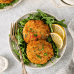 a plate of greens topped with two air fried frozen crab cakes.