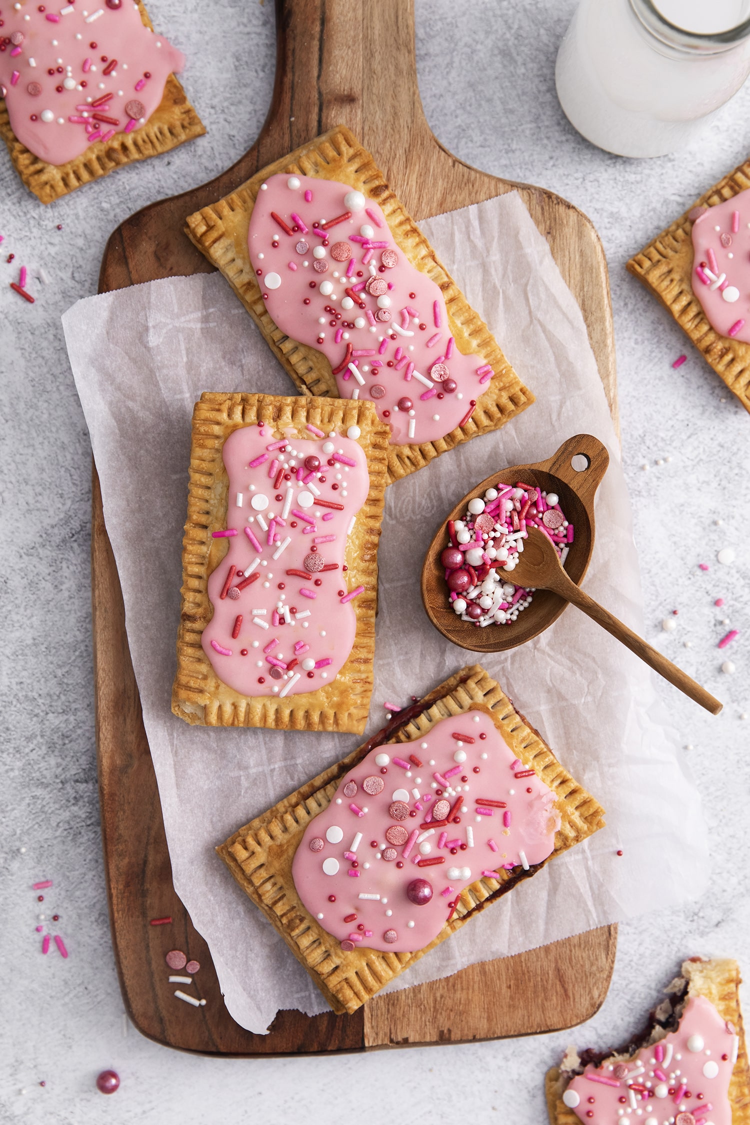 a large wooden board holding homemade air fried pop tarts covered in pink sugar glaze and fun spinkles.
