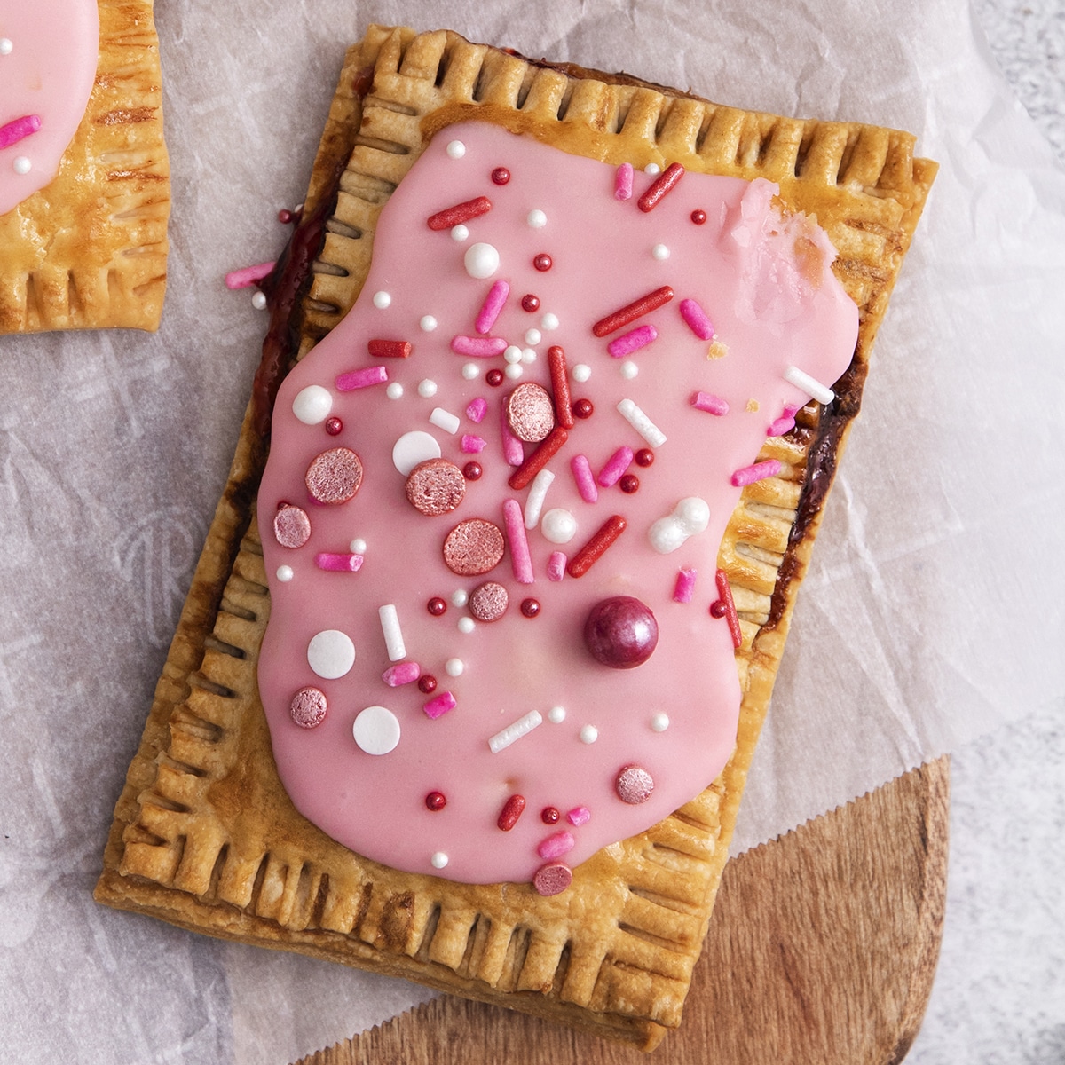 a homemade pastry air fryer pop tart with pink frosting and sprinkles, on parchment paper