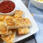 horizontal photo of a pile of slices of air fryer cheesy bread on a white plate with a bowl of dip also on the plate