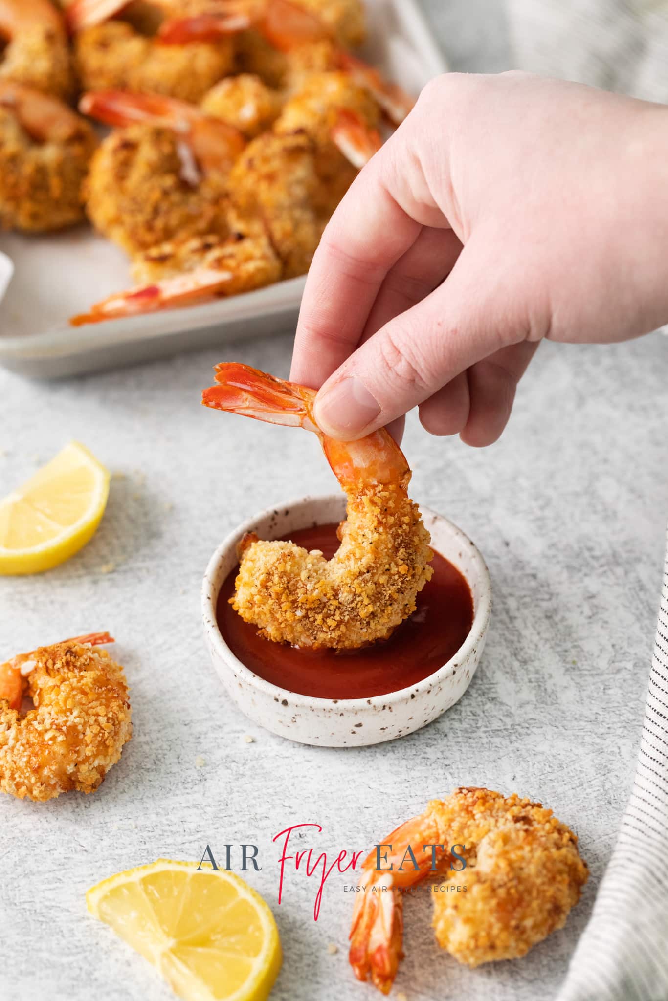 a hand dipping a breaded shrimp into a bowl of cocktail sauce.