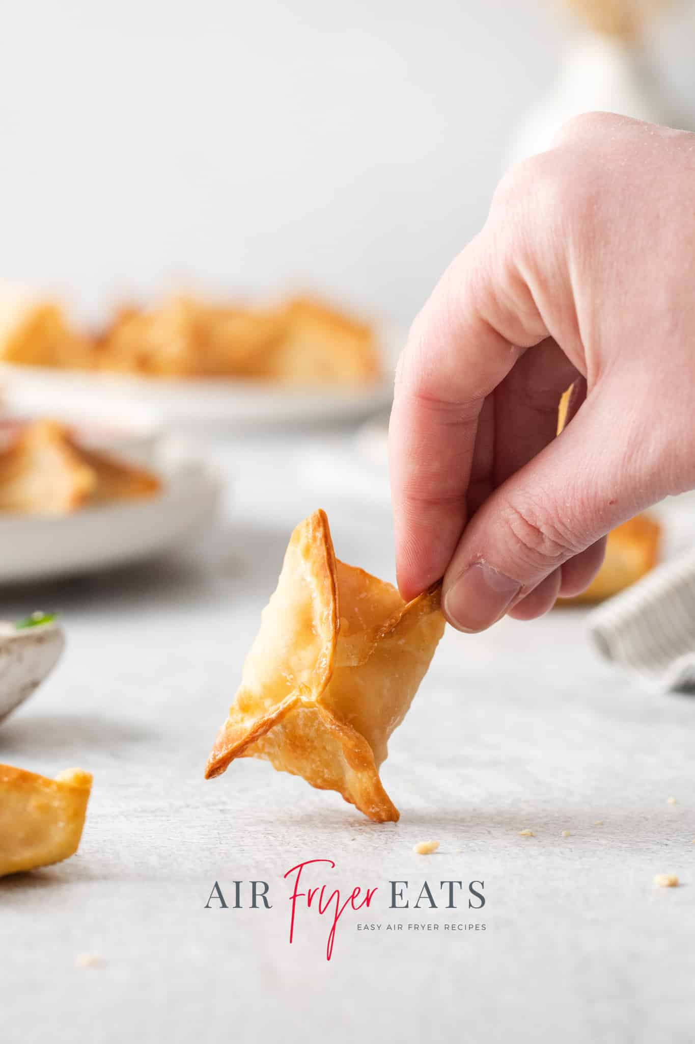 a hand holding an air fried crab rangoon that is in a pillow shape with crispy seams.