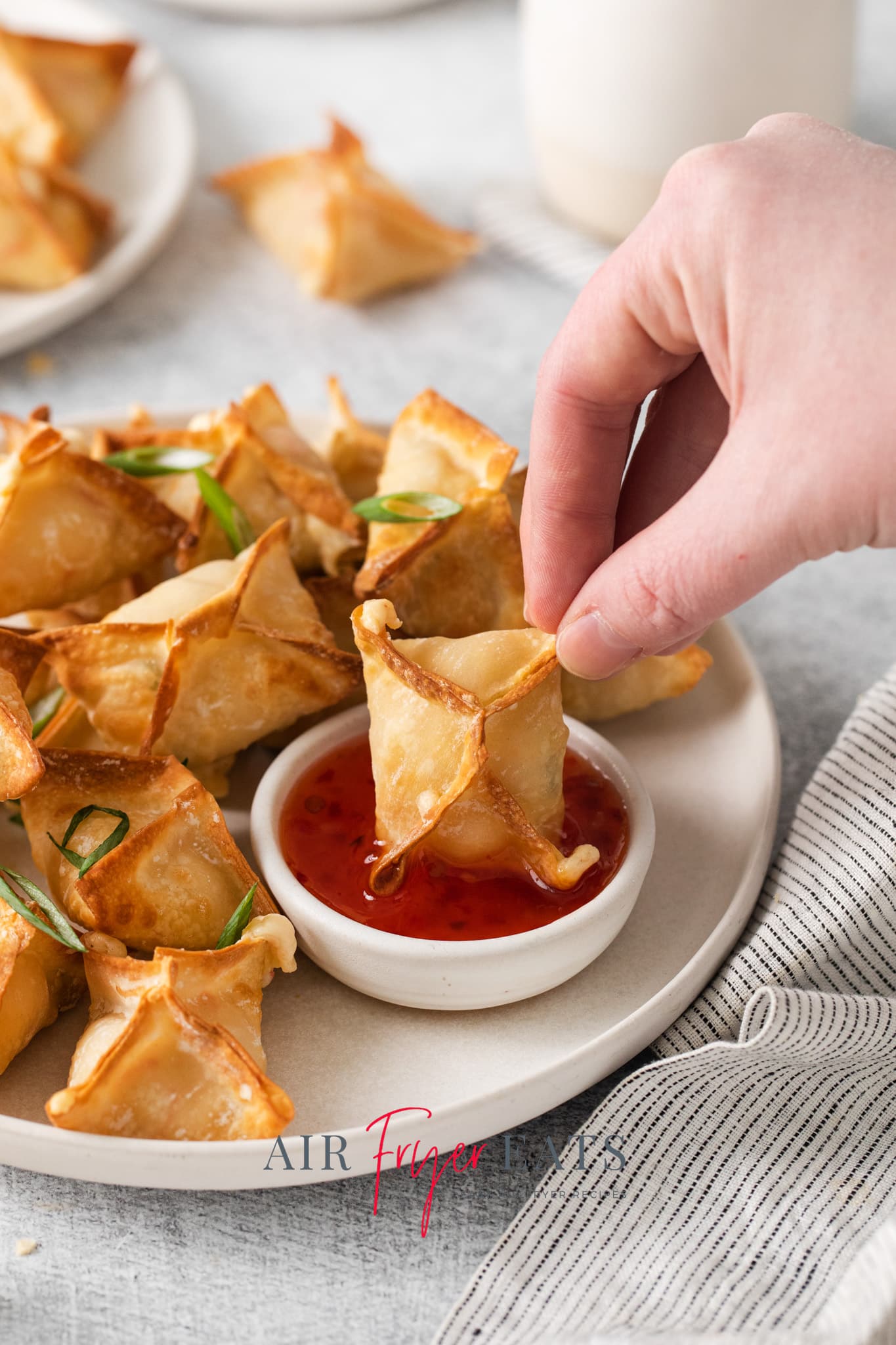 a platter of crab rangoons. A hand is dipping one into sweet and sour sauce.