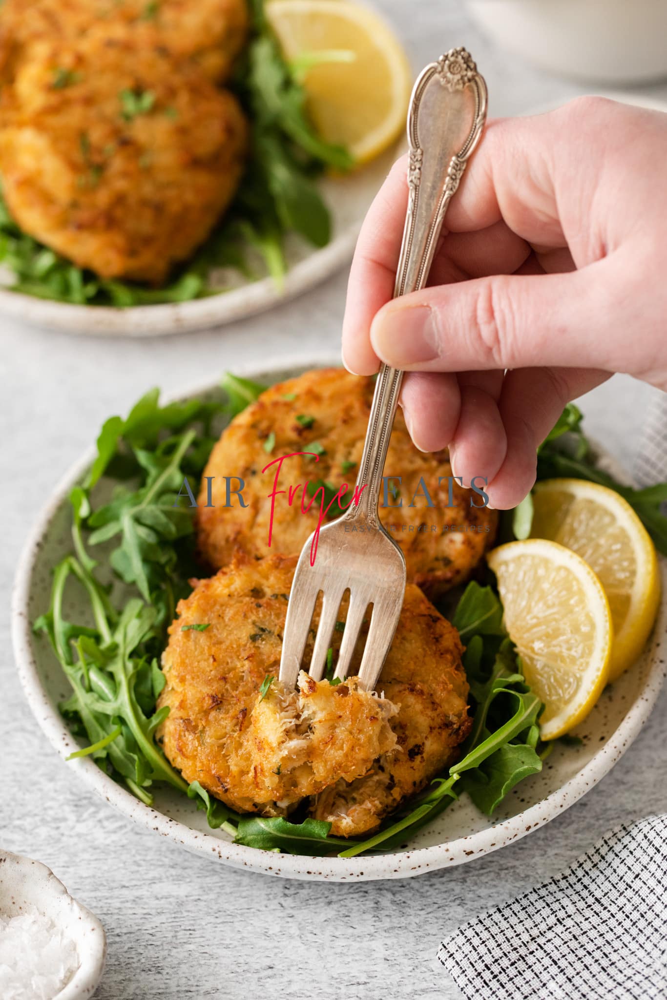 a plate of crab cakes and lettuce. A hand is eating one with a fork. 