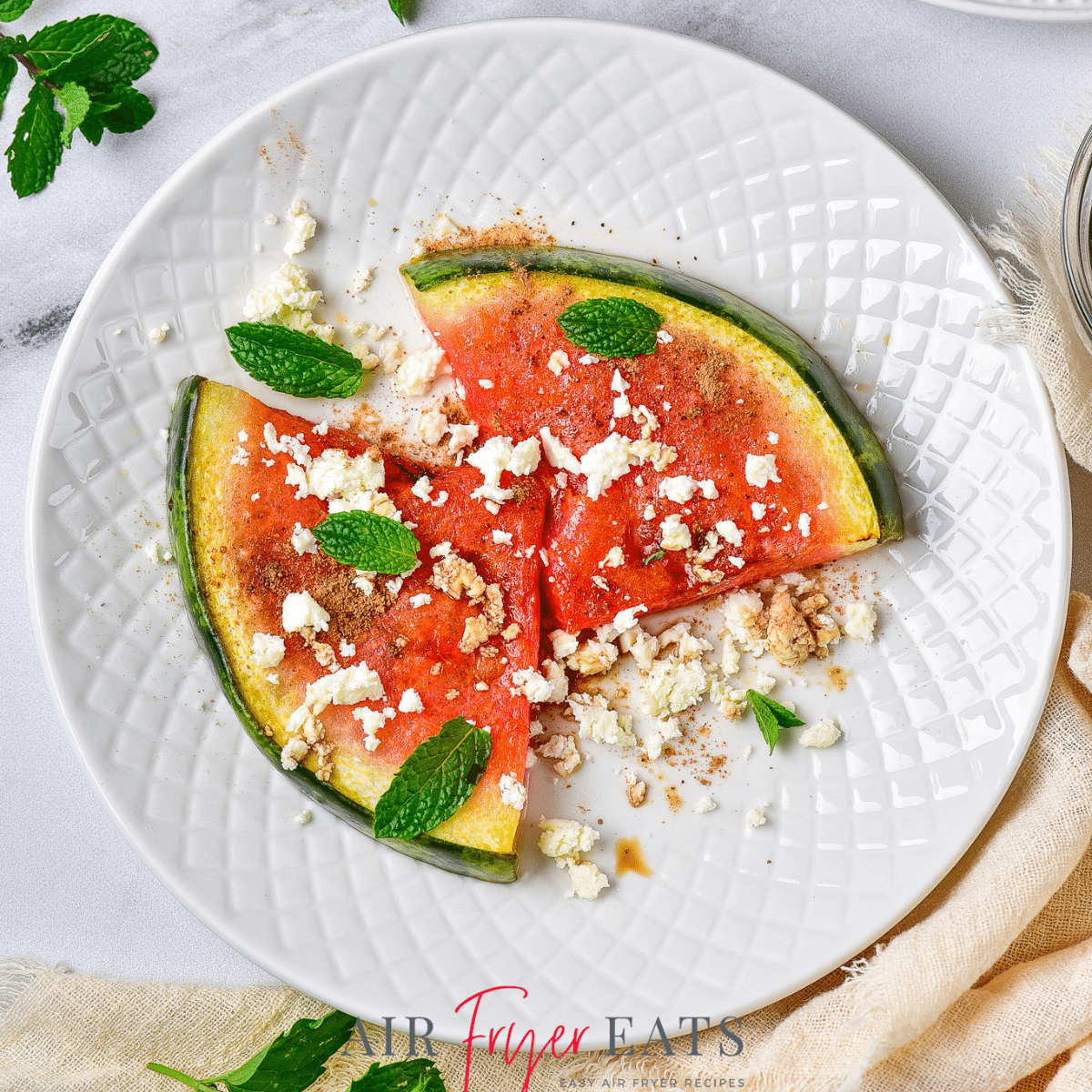 two pieces of air fried watermelon topped with fresh mint and feta cheese, on a plate.