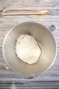vertical photo showing a dough ball in a greased mixing bowl. The dough ball has doubled in size. On a wooden surface