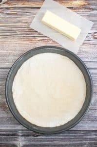vertical photo showing the pizza base pressed down into the bottom of a pie pan