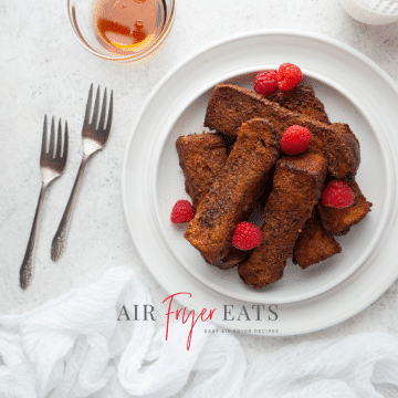 a plate of french toast sticks with raspberries. Two forks are next to the plate.