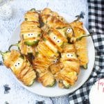 horizontal photo of a pile of Air Fryer Mummy Poppers on a white plate with toy spiders around the plate