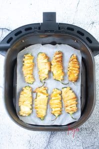 vertical photo of an air fryer basket on a white marble surface with cooked Air Fryer Mummy Poppers inside
