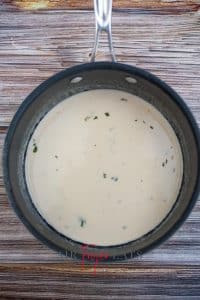 vertical photo of a saucepan with wine, garlic, chives, cilantro, and butter reduced down, and cream added