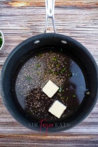 vertical photo of a saucepan with wine, garlic, chives, cilantro, and butter added