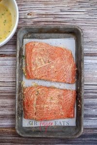 vertical photo of two salmon fillets coated with garlic butter placed in the prepared tray