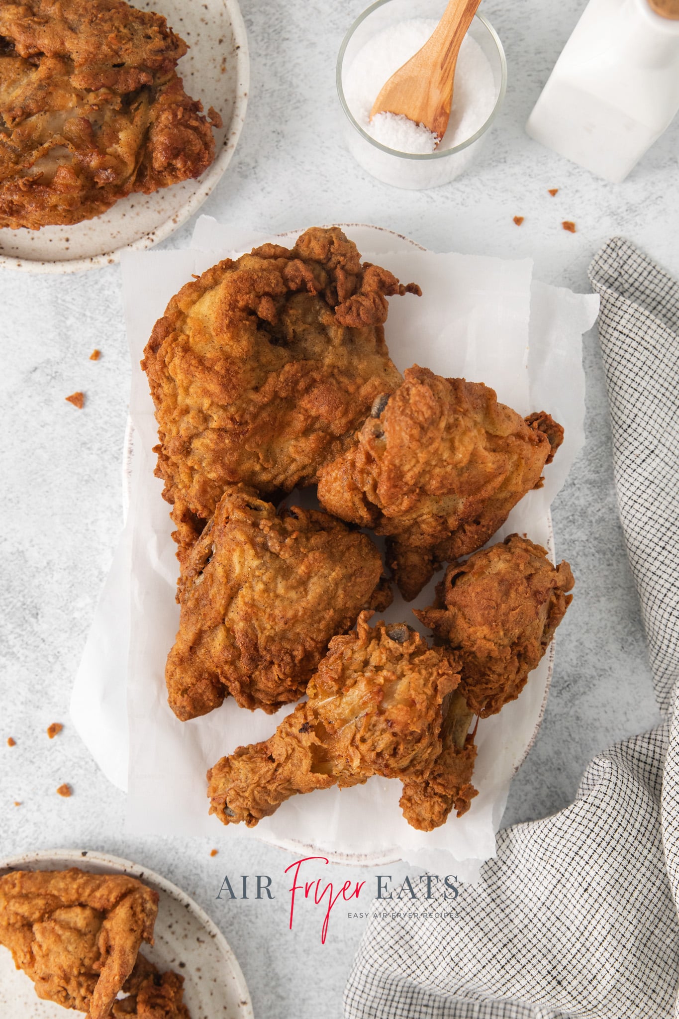 a platter lined with parchment paper, filled with mixed pieces of leftover fried chicken.