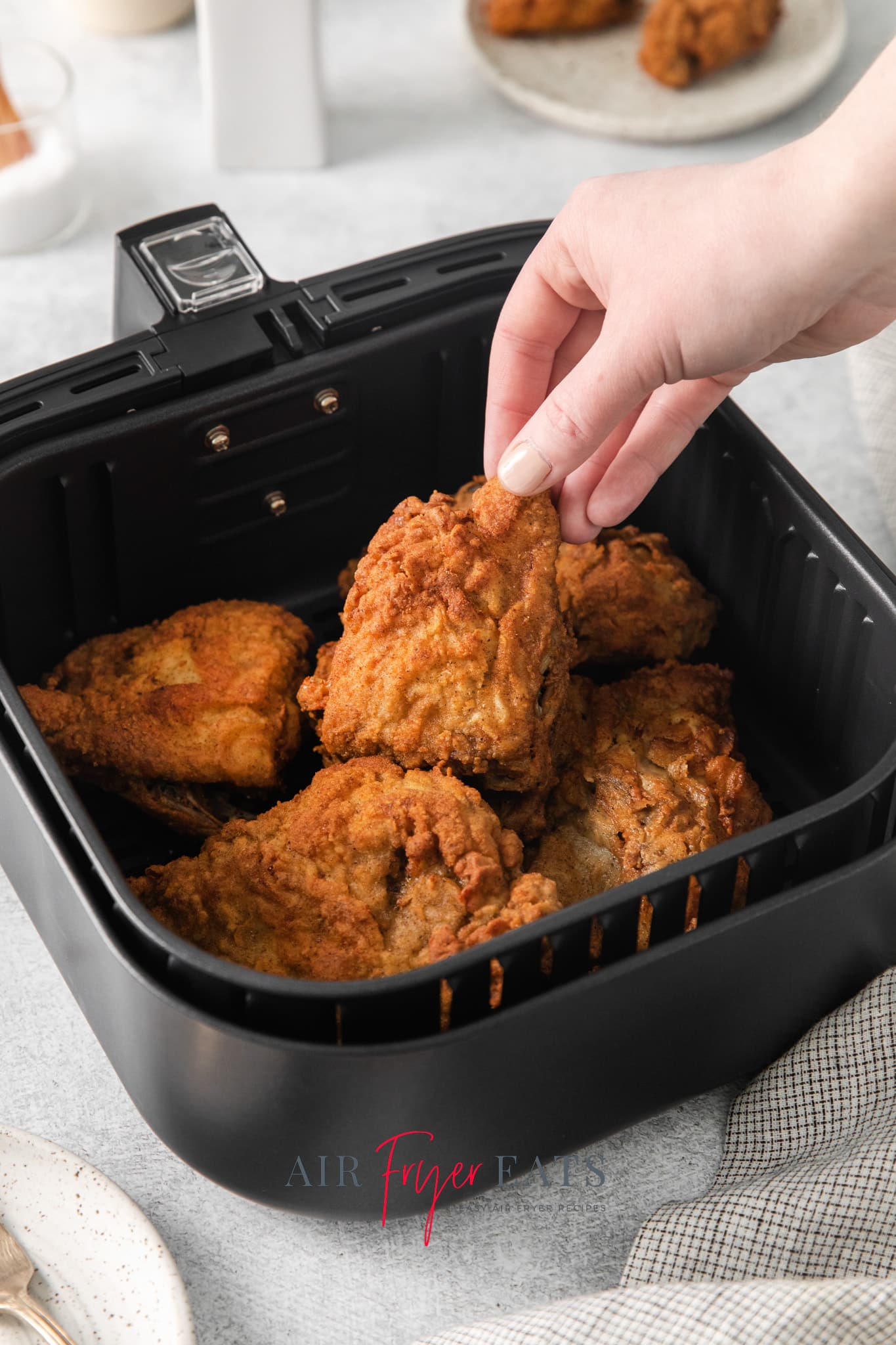 a hand picking up reheated fried chicken from the air fryer.