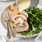 sliced air fryer chicken cordon bleu on a plate with greens. Sauce is being poured over the chicken.