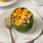 a green stuffed pepper topped with melted cheese on a plate with a fork.
