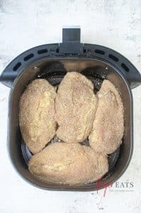 vertical overhead photo of four pieces of Jalapeno Popper Stuffed Chicken in an air fryer basket ready to be cooked