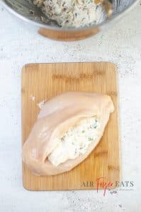 vertical photo of a sliced and stuffed chicken breast on a wooden cutting board