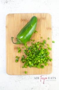 vertical photo of a cutting board with a whole jalapeno and some diced jalapeno