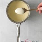 creamy dijon sauce cooking in a saucepan. A spoon is coated with the sauce.