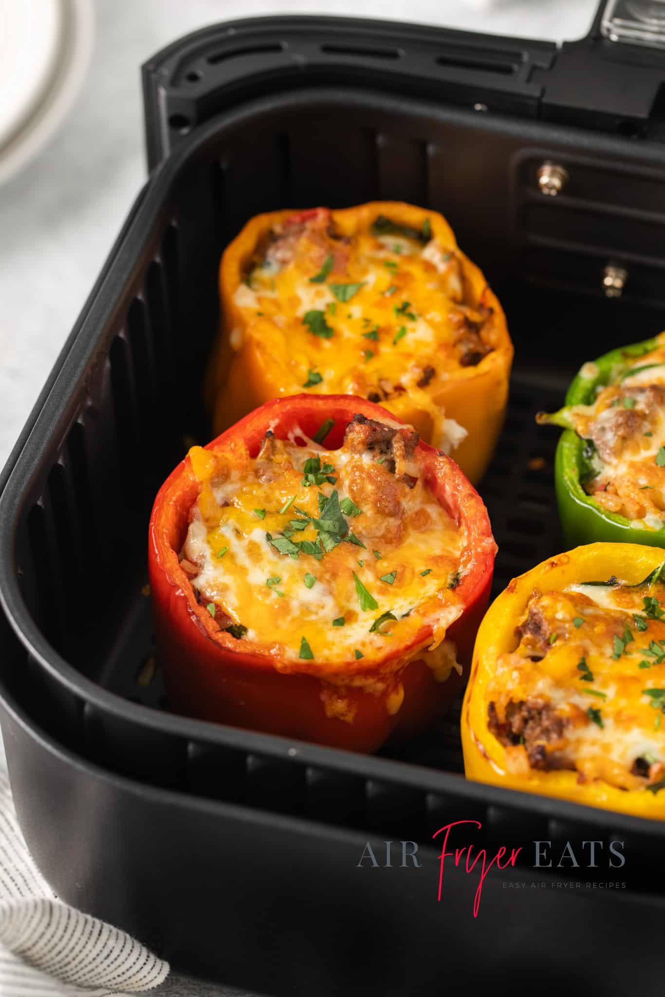 stuffed peppers topped with melted cheese, in a black air fryer basket.