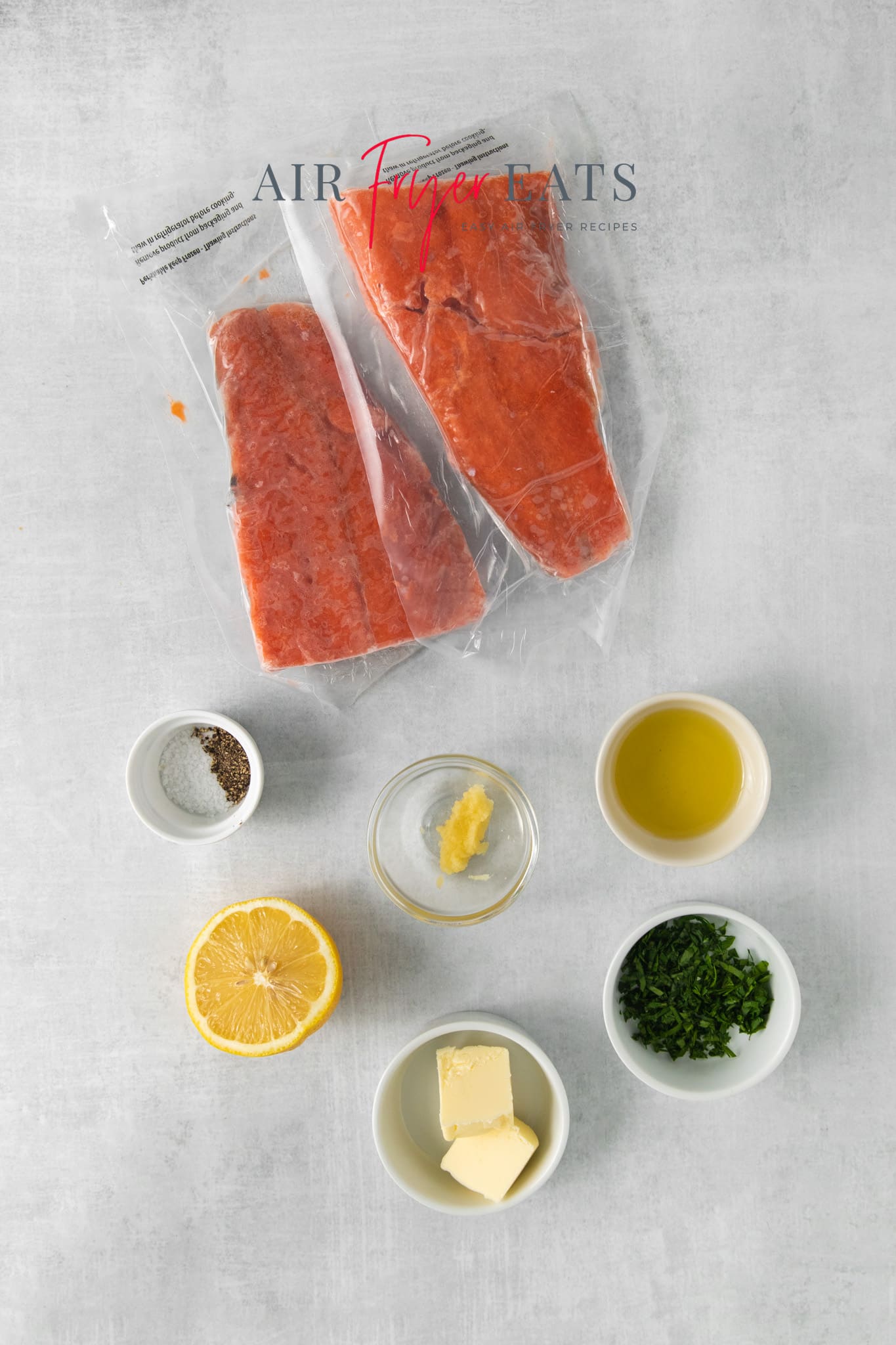 two frozen salmon filets on a counter with the ingredients needed to cook them in the air fryer.