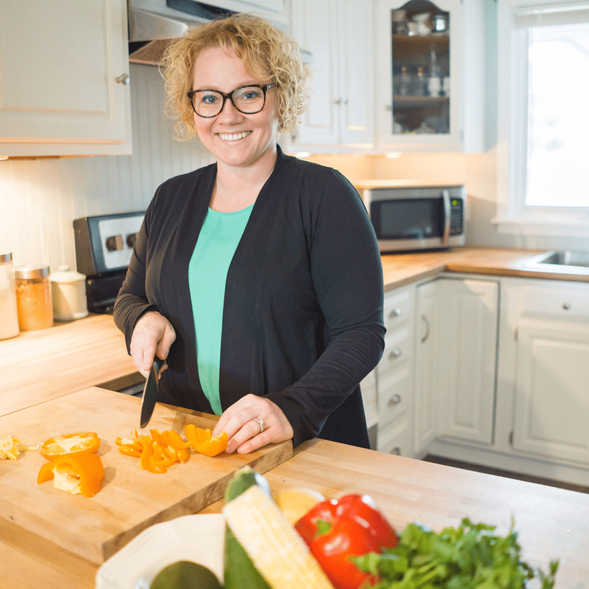 Cindy gordon wearing a black shirt and a green shirt dicing vegetables on a cutting board in a kitchen