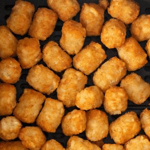 closeup of crispy tater tots in an air fryer basket.