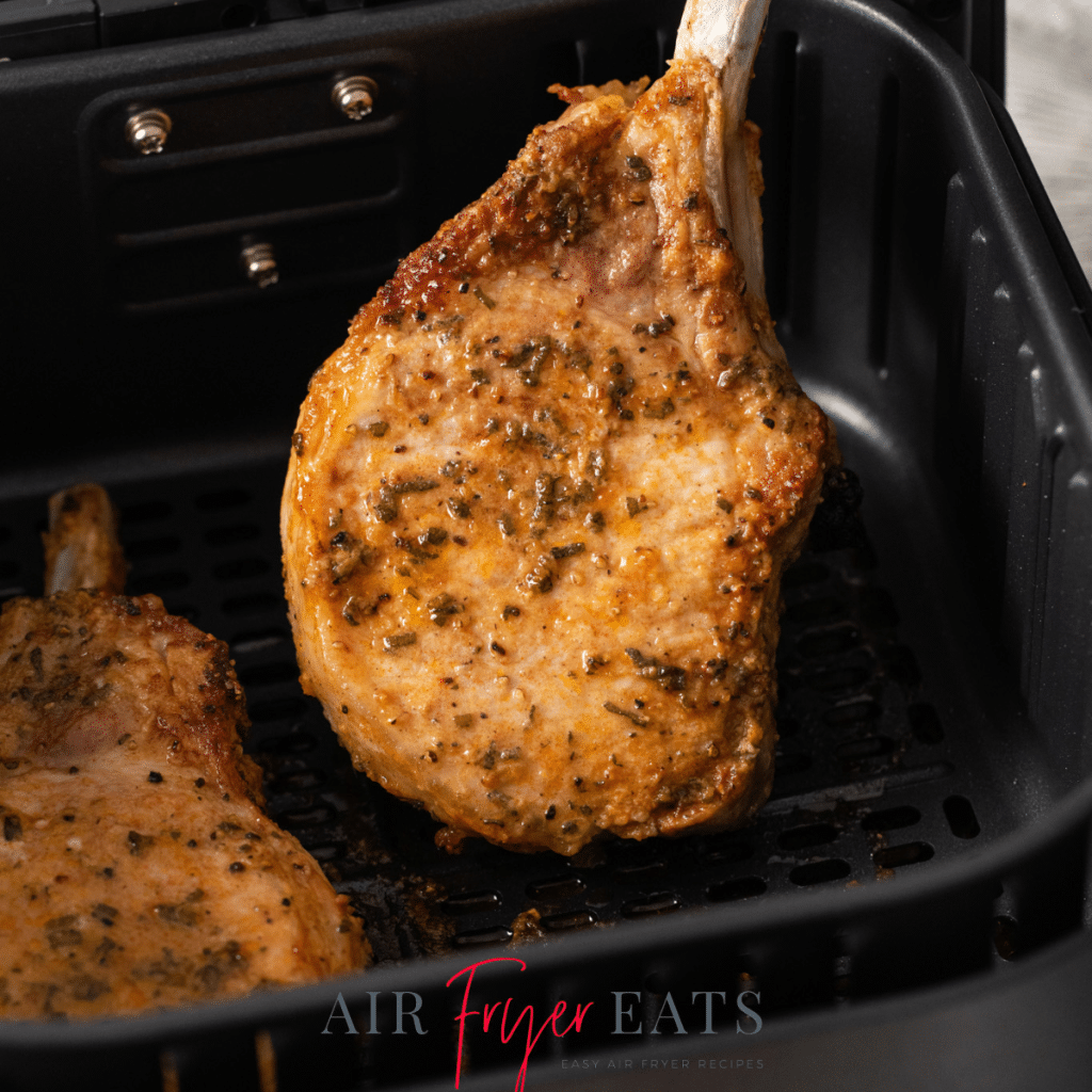 a bone in pork chop held up out of an air fryer basket.