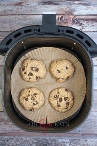 vertical photo of an overhead shot of an air fryer basket with four cooked air fryer chocolate chip oatmeal cookies