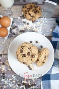 vertical photo of 2 air fryer chocolate chip oatmeal cookies on a plate with other ingredients around the plate