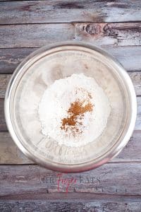 vertical photo of an overhead shot of a bowl with flour, baking soda, cinnamon and salt