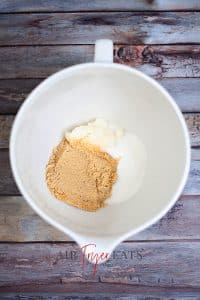 vertical photo of an overhead shot of a bowl with brown sugar, white sugar and coconut oil