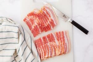 Raw bacon is placed on a cutting board and has been sliced in half.