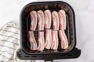 Slices of bacon are arranged neatly in an air fryer basket.