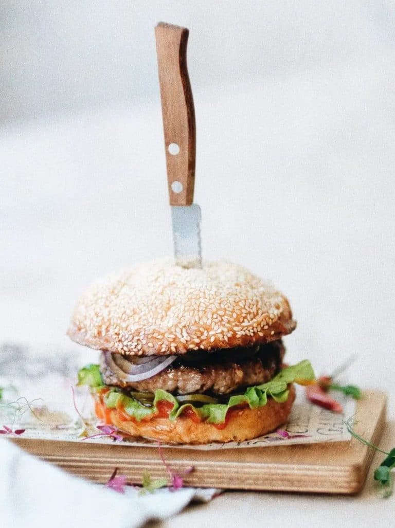 Air fryer frozen hamburger is placed on a cutting board with a wooden-handled knife in the center. The burger has lettuce, onions, and a juicy patty.