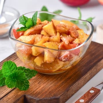 an image of air fryer fried apples sitting in a clear glass bowl. The bowl is sitting on a wooden cutting board.
