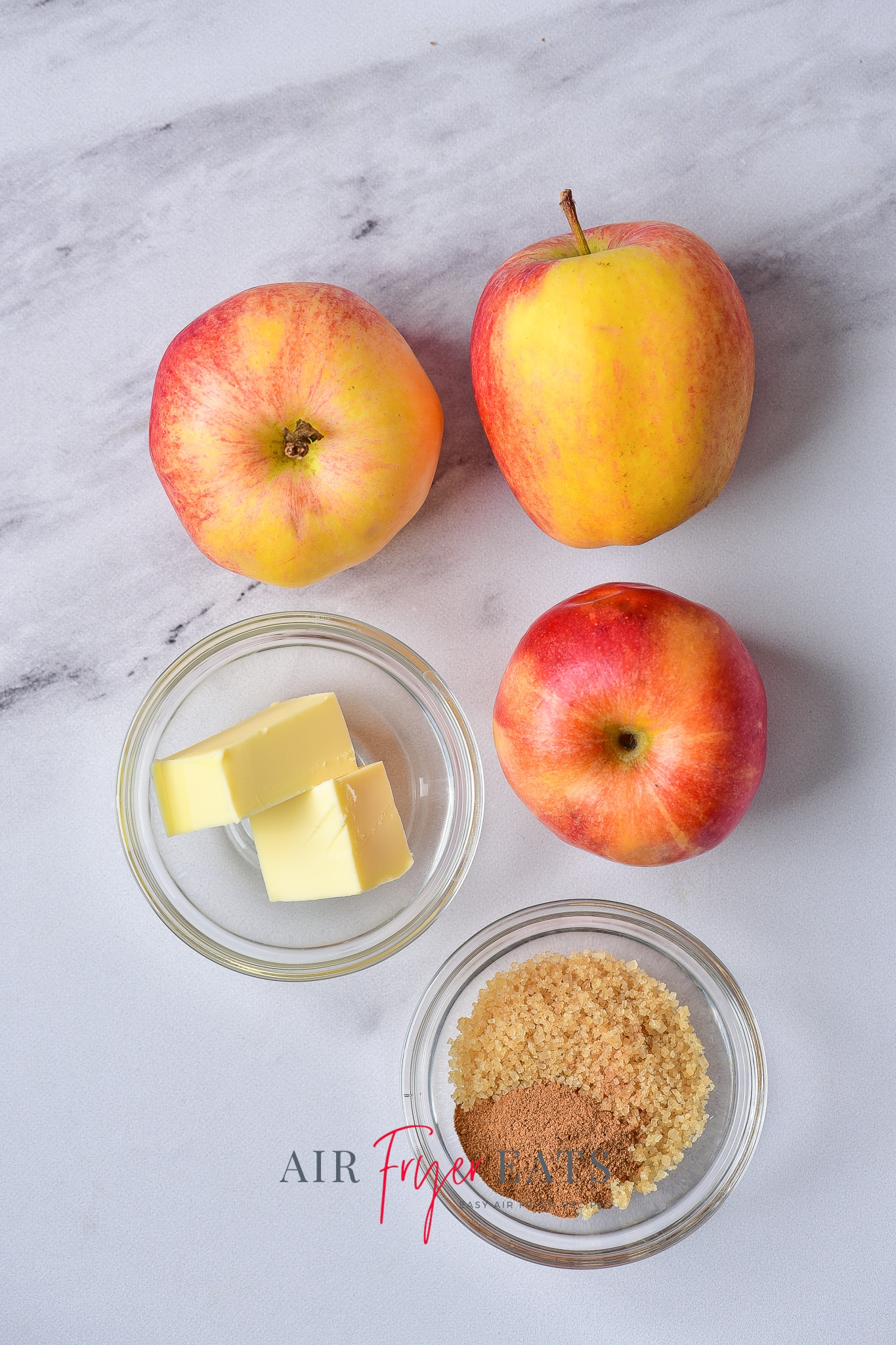 a picture showing the ingredients needed to make air fryer fired apples. The ingredient are sitting on a white, marble countertop.