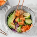 A close up picture of an air fryer poke bowl. Someone is reaching into the bowl with a pair of chopsticks and grabbing a piece of tofu.