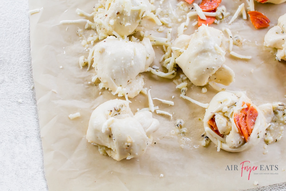 Garlic knot pizza dough filled with mozzarella cheese, pizza sauce, and pepperoni, ready to be cooked in the air fryer.