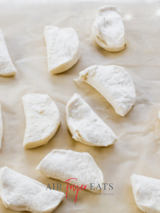 Canned biscuit dough is cut in half for air fryer garlic knot pizza.