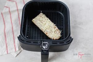 One piece of frozen Stouffer’s French bread pizza lies in a black air fryer basket.