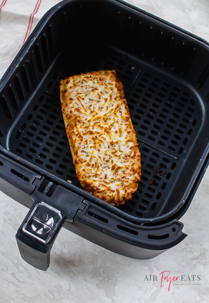 One piece of cooked Stouffer’s French bread pizza lies in a black air fryer basket. The cheese pizza is golden-brown and crispy.